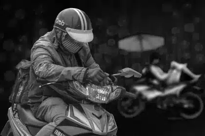 Coursier à scooter livrant sous la pluie dans une rue urbaine avec restaurants et immeubles